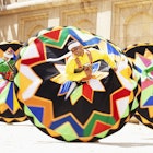A trio of men twirl in large colorful skirts.